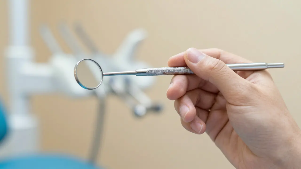 Ruka zubního lékaře držící ergonomické dentální zrcátko